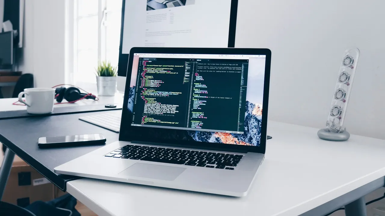 A laptop showing code on a desk, natural light from a window